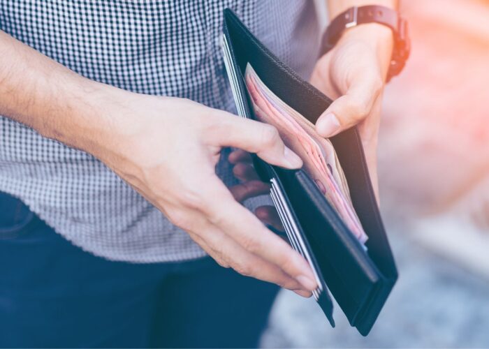 Man standing holding black wallet full of money.