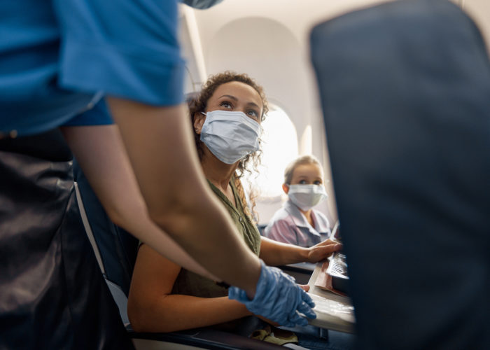 Woman and child wearing masks on plane speaking to a flight attendant