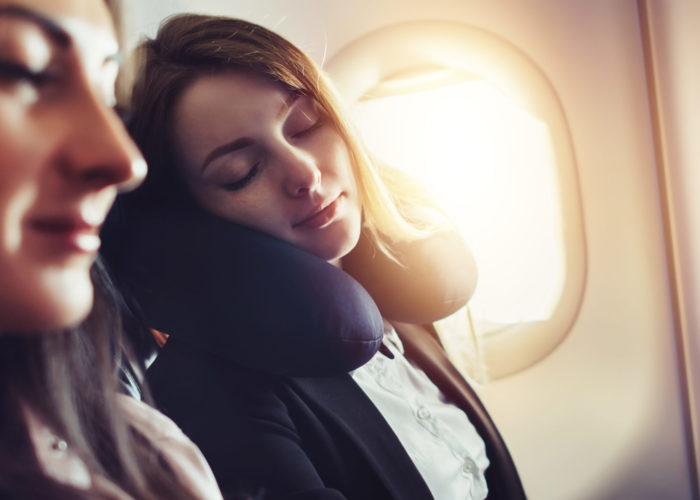 Woman sleeping using a neck pillow in a window seat on an airplane
