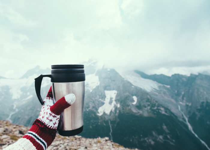 Point of view shot of a person holding a thermos of tea against a mountain backdrop