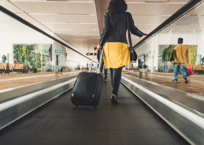 Woman rolling a suitcase down an automatic walkway in an airport